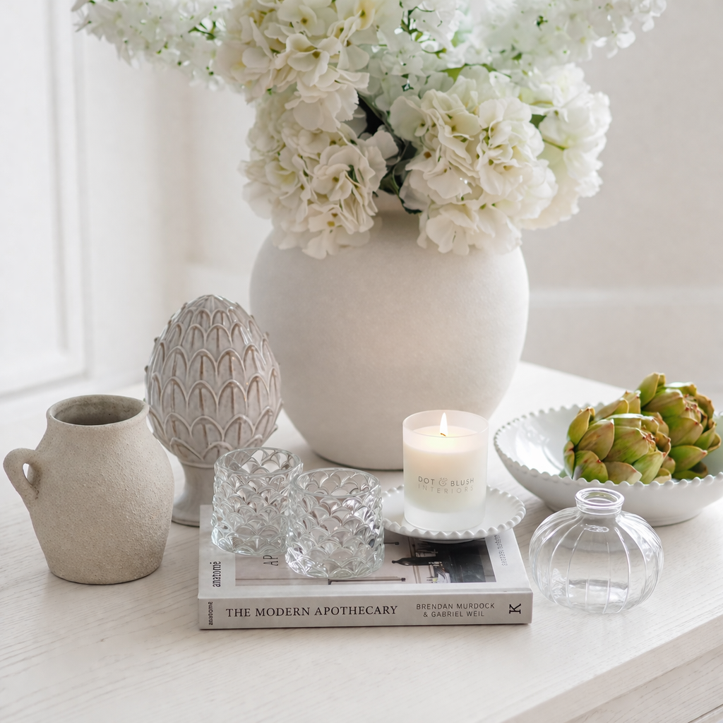 Decorative setting with a vase of white flowers, candles, and books on a table.