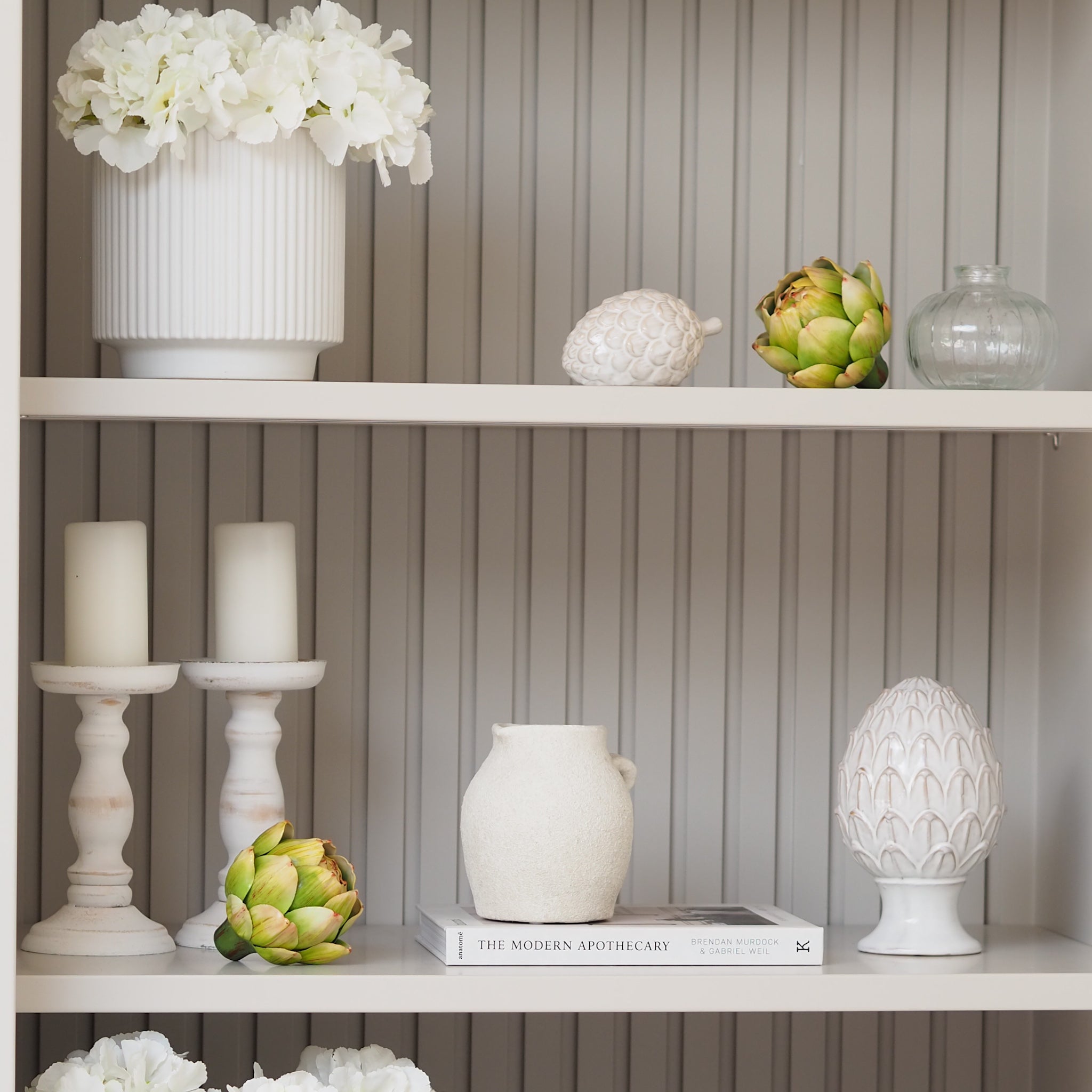 Decorative shelf with white vases, candles, and artichokes against a striped wall.