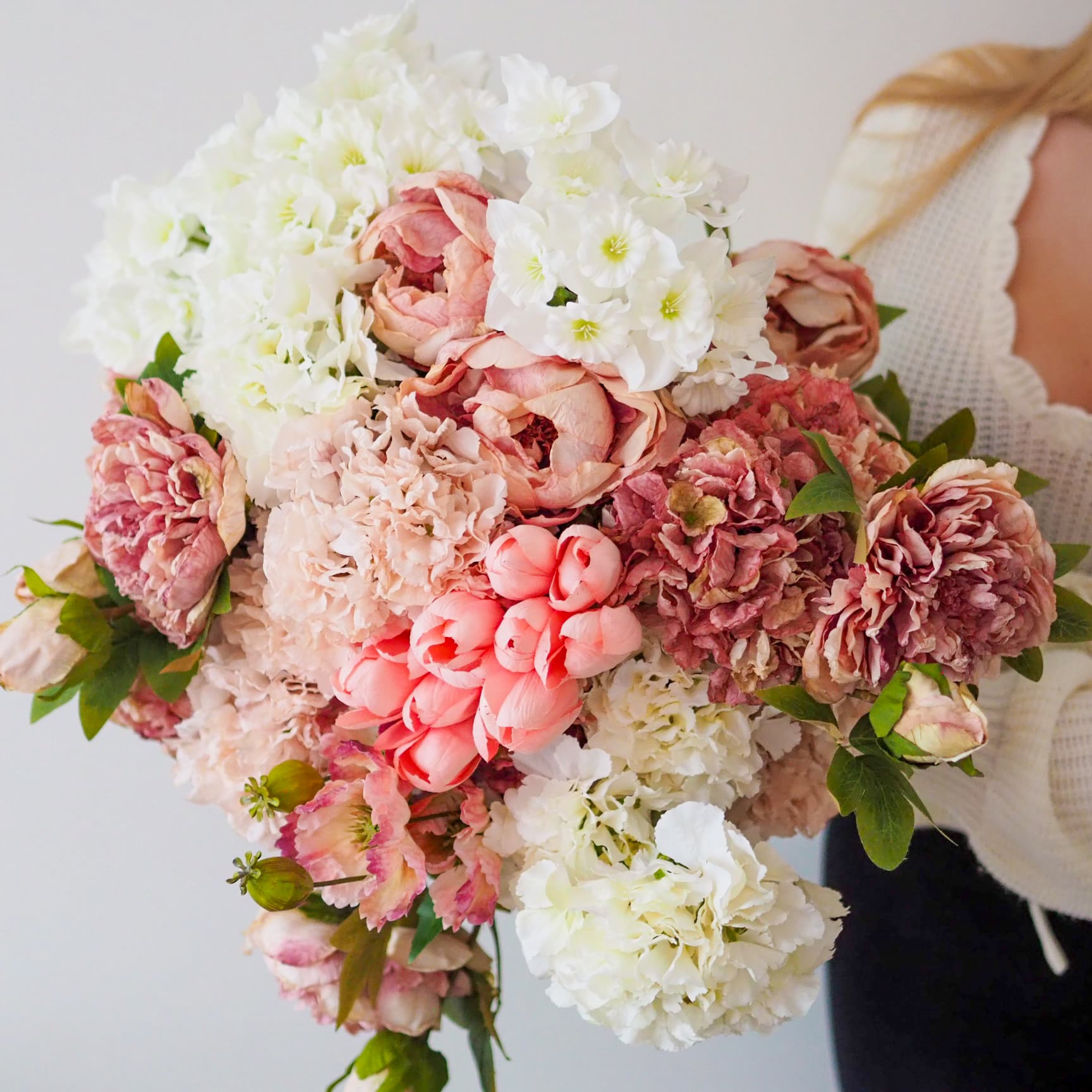 Bouquet of pink and white faux flowers held by a woman wearing a cream jumper.