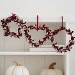 A fall-themed garland with burgundy leaves and gold berries hangs across a white shelf, flanked by white and cream pumpkins below.