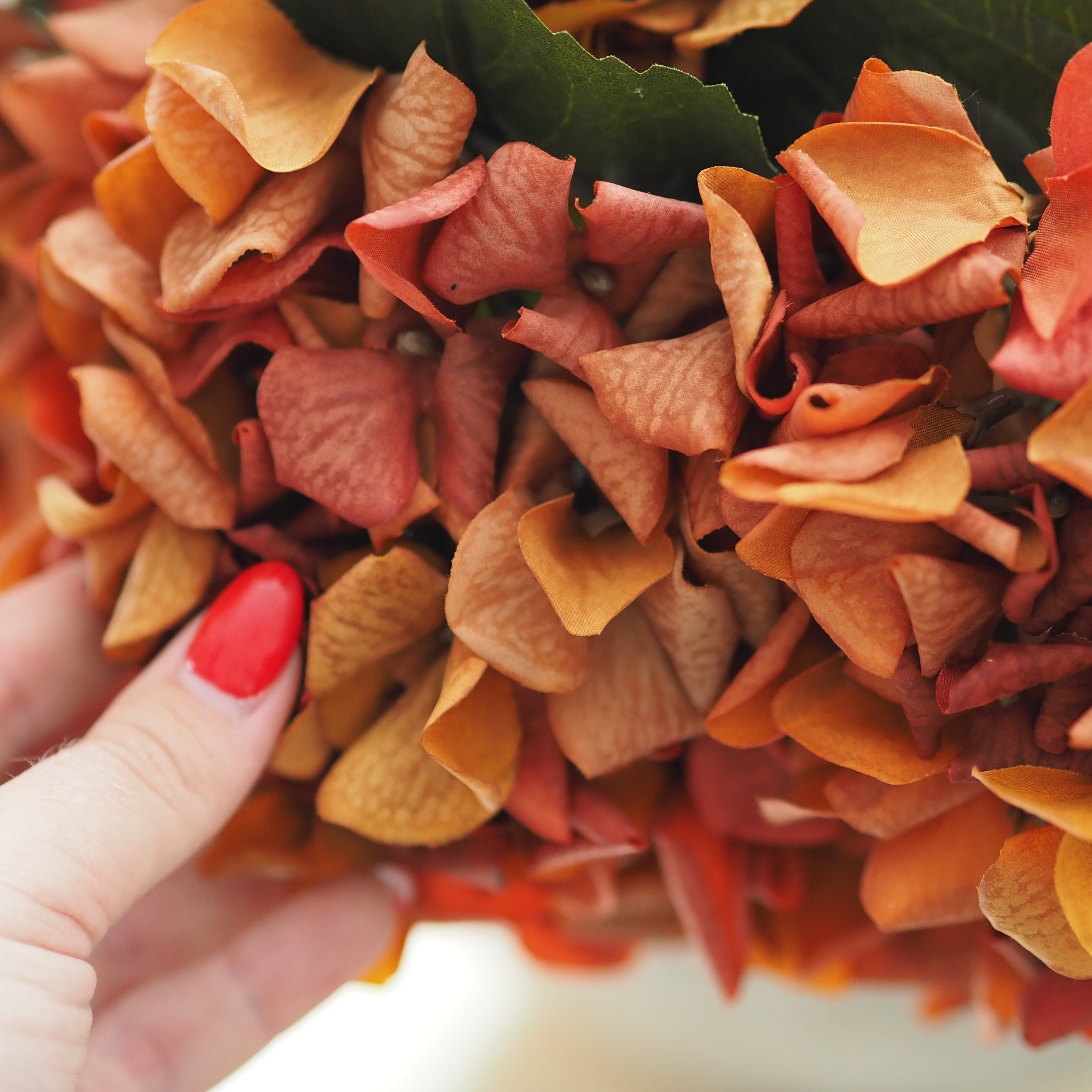 cluster of artificial autumn hydrangea style flowers in warm orange, peach, and rust tones with a few dark green leaves visible.