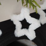 A fluffy white faux-fur star-shaped garland hanging near green pine branches against a light wall and dark surface.