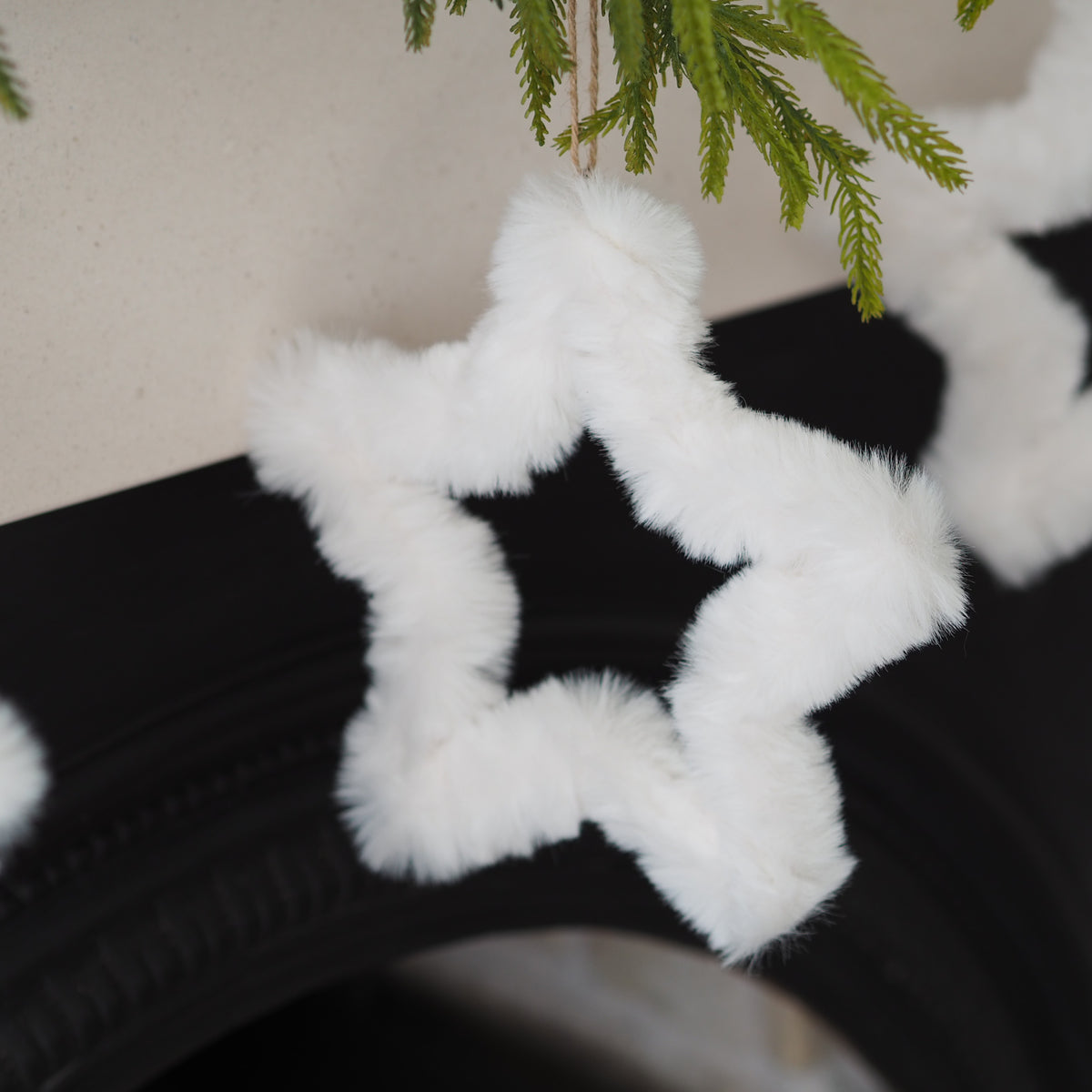 A fluffy white faux-fur star-shaped garland hanging near green pine branches against a light wall and dark surface.