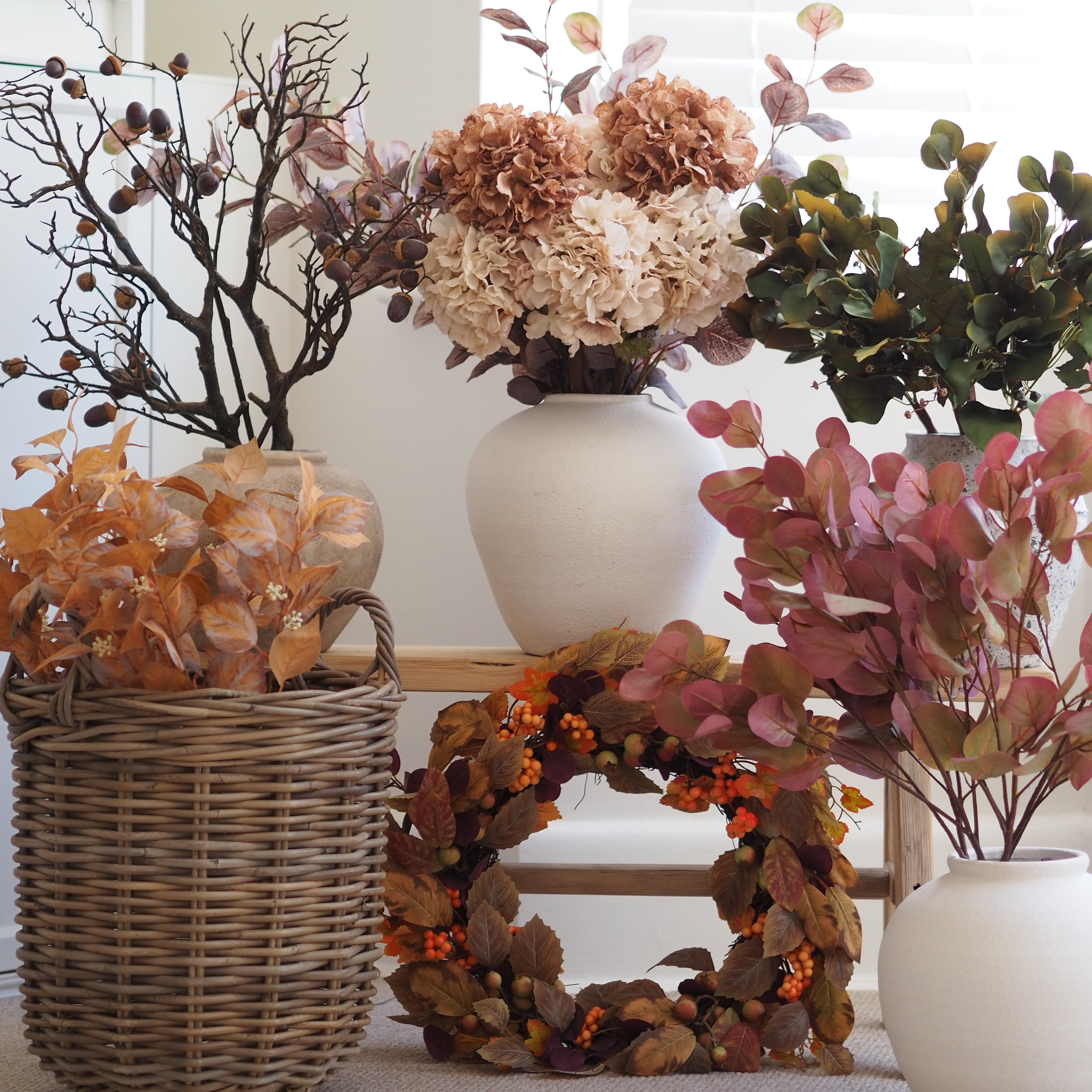 Autumn floral arrangement set featuring faux hydrangeas, eucalyptus, berries, and a leaf wreath in wicker and ceramic vases.