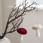Two mushroom-shaped fabric ornaments in deep burgundy and cream, hanging from a decorative bare tree branch in a light-colored ceramic vase. Autumn decor Inspo 